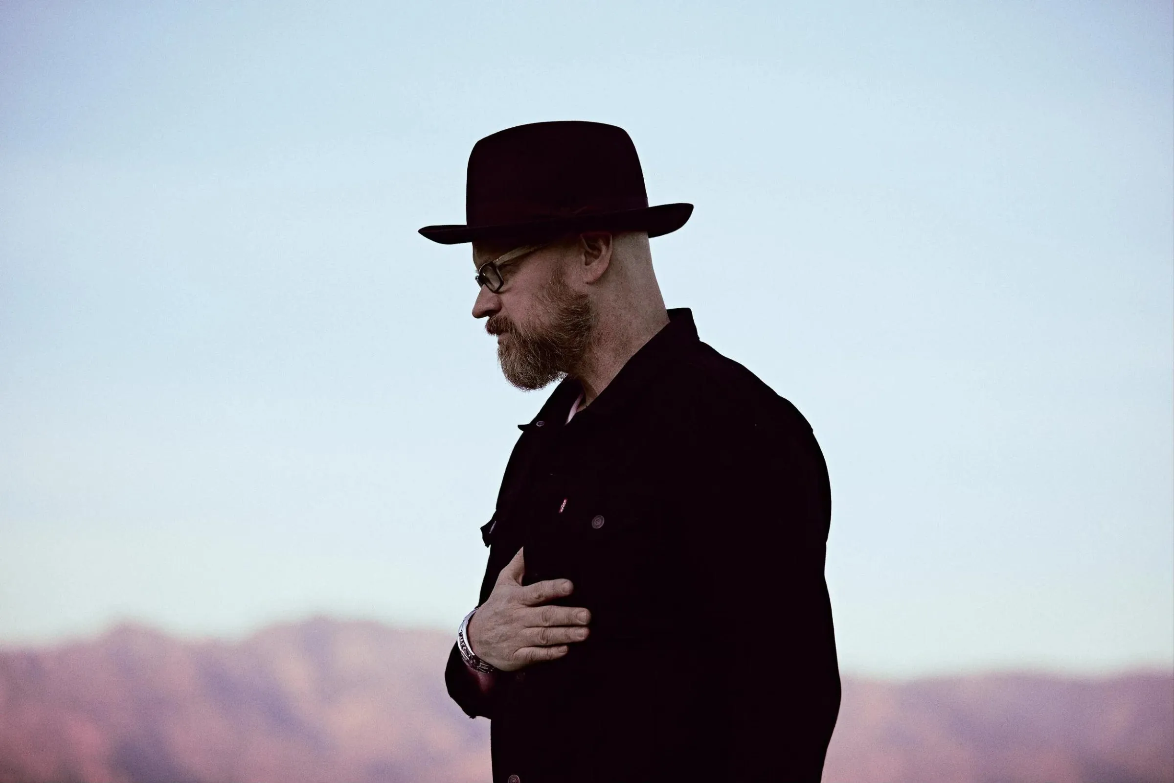 Anthony Skinner in silhouette at dusk with his hand over his heart, desert mountains behind him